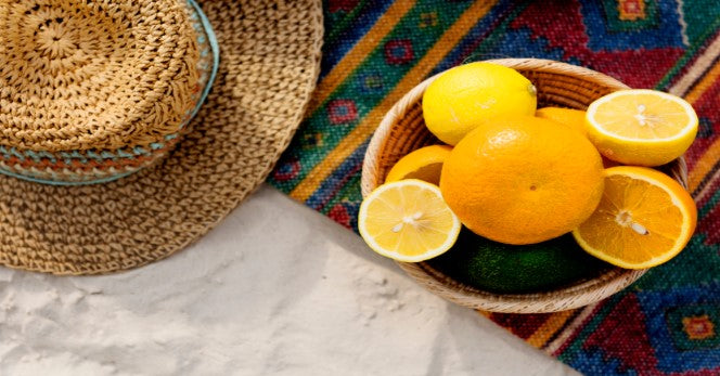 A summer hat resting beside fresh oranges rich in vitamin C, symbolizing health and sunny vibes.